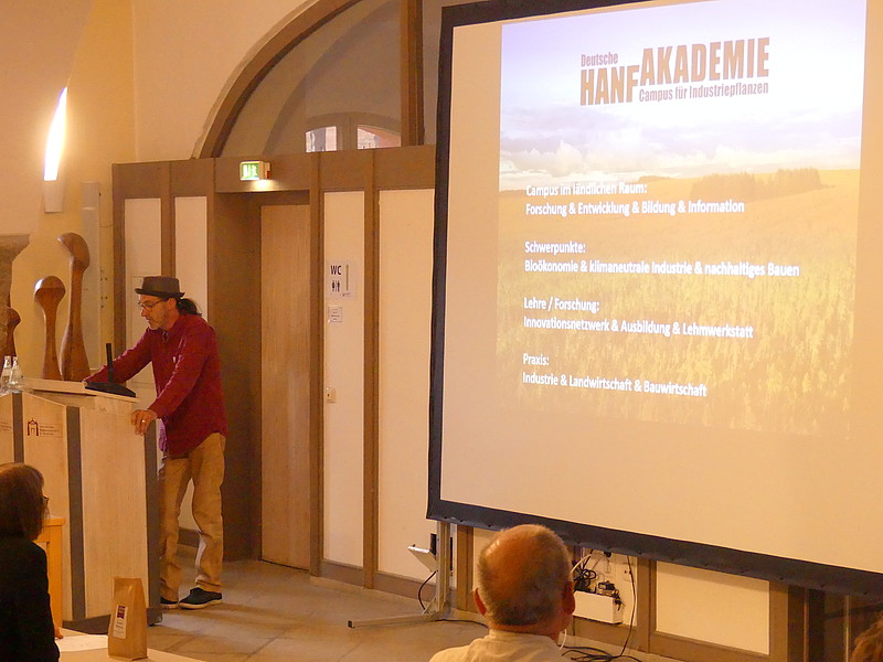 Herr Thom Nowotny von der Deutschen Hanf-Akademie e. V. hält mit Präsention im Hintergrund einen Vortrag