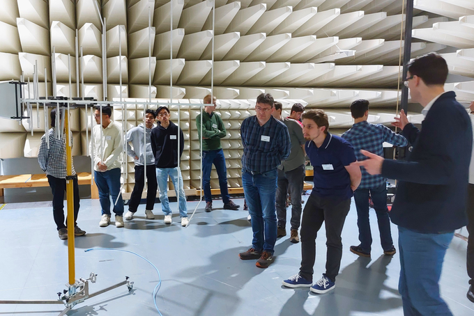 Mehrere Personen stehen in einem großen Raum mit einer Messeinrichtung und mit Klangabsorptionsmaterial