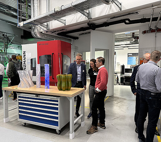Gäste und Mitarbeitende im Gespräch im Technikum vor Demonstratoren und 3D-gedruckten Gegenständen.