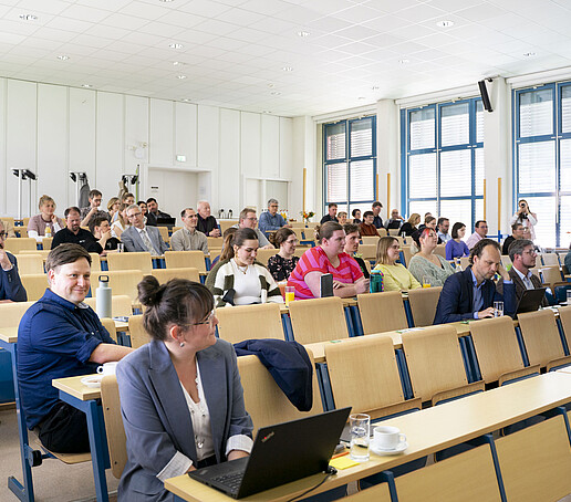 Menschen sitzen auf den Stuhlrängen im Vorlesungssaal.