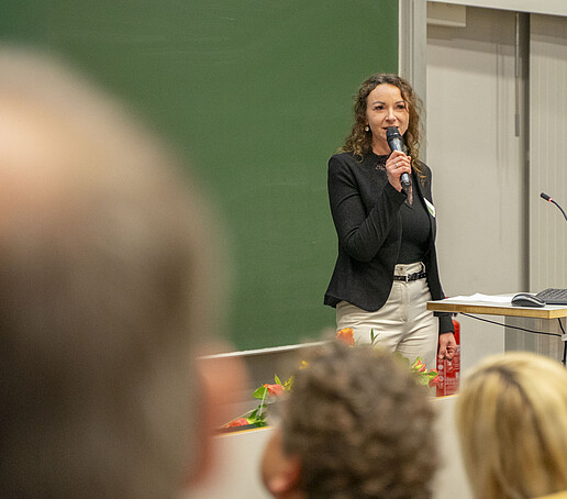 Eine Frau spricht in ein Mikrofon vor dem Publikum.