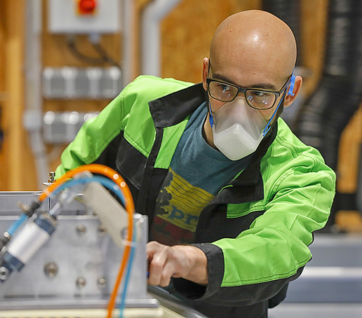 Mann arbeitet mit Mund-Nasen-Maske an einer Maschine
