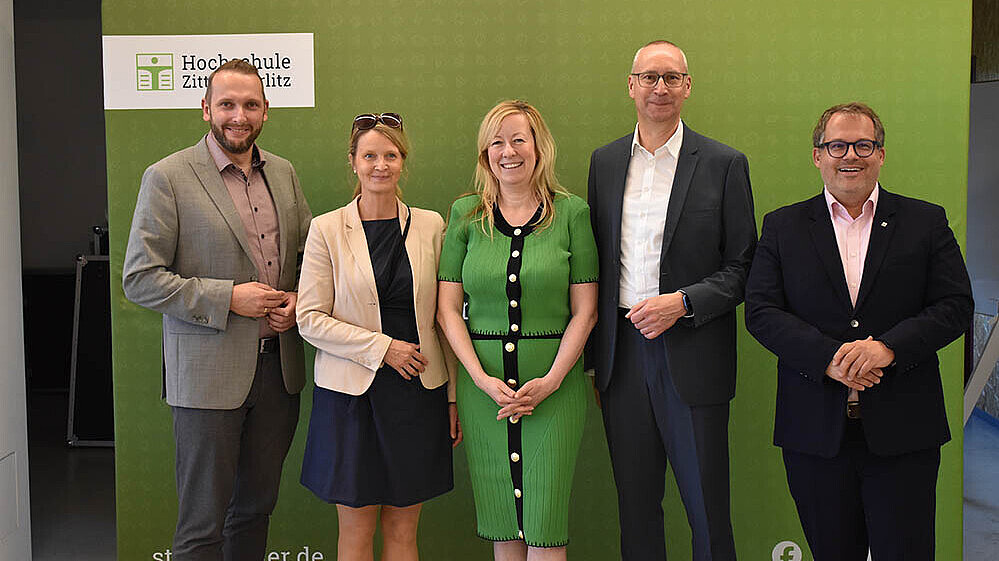 Eine Delegation der HSZG und der Stadt Bautzen steht vor der grünen Pressewand und lächelt in die Kamera.
