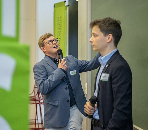 Zwei junge Wissenschaftler erläutern ihr Projekt an einer grünen Tafel.