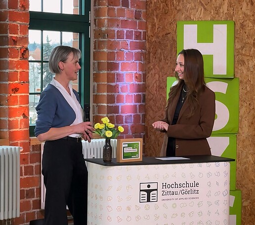 Die Prorektorin Bildung und die Moderatorin stehen hinter der Messetheke im TV-Studio.