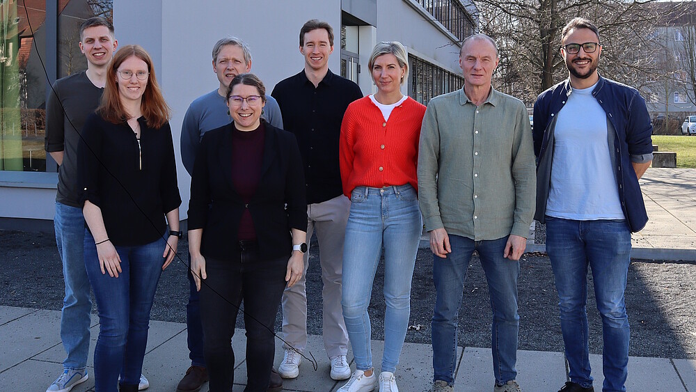 Acht Mitglieder der Nachwuchsforschergruppe „Toolbox Biomedizin“ stehen bei sonnigem Wetter vor einem Hochschulgebäude auf dem Campus der Hochschule Zittau/Görlitz und blicken in die Kamera.