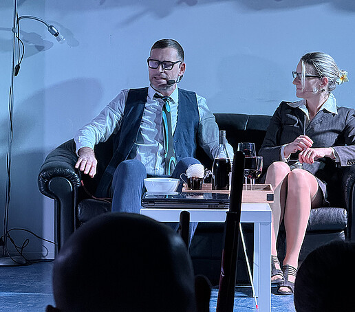 Zwei Darsteller sitzen auf der Couch.